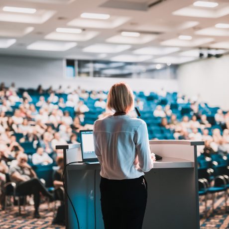 Female speaker giving a talk on corporate business conference. Unrecognizable people in audience at conference hall. Business and Entrepreneurship event